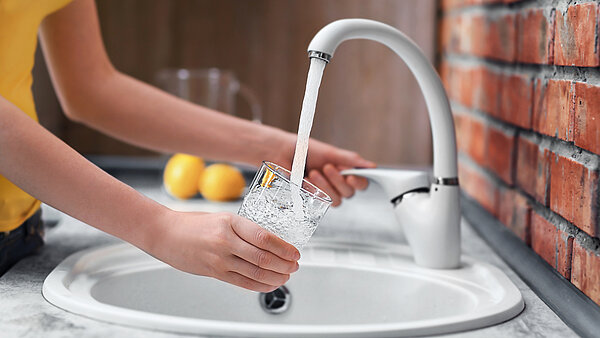 Glas wird am Wasserhahn mit Trinkwasser befüllt